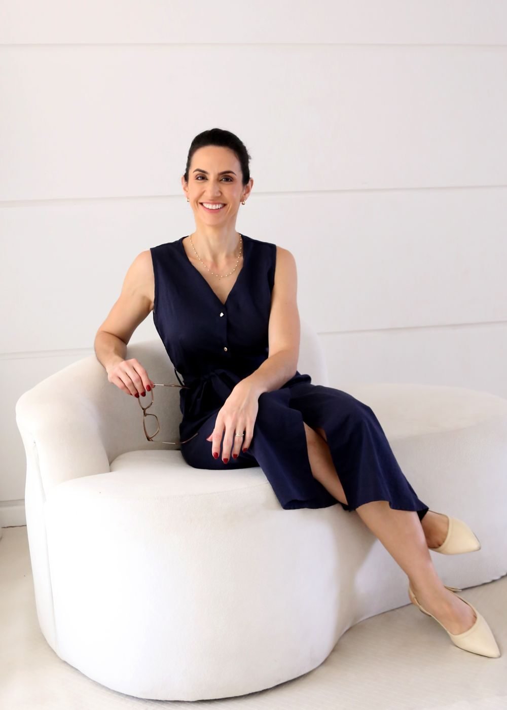 Dra. Svenja Lopez, cirurgiã plástica, sentada em poltrona branca no consultório