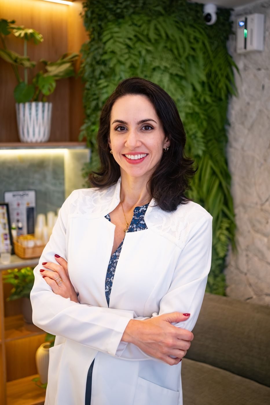 Dra. Svenja Lopez de jaleco branco, braços cruzados, sorrindo na recepção do consultório
