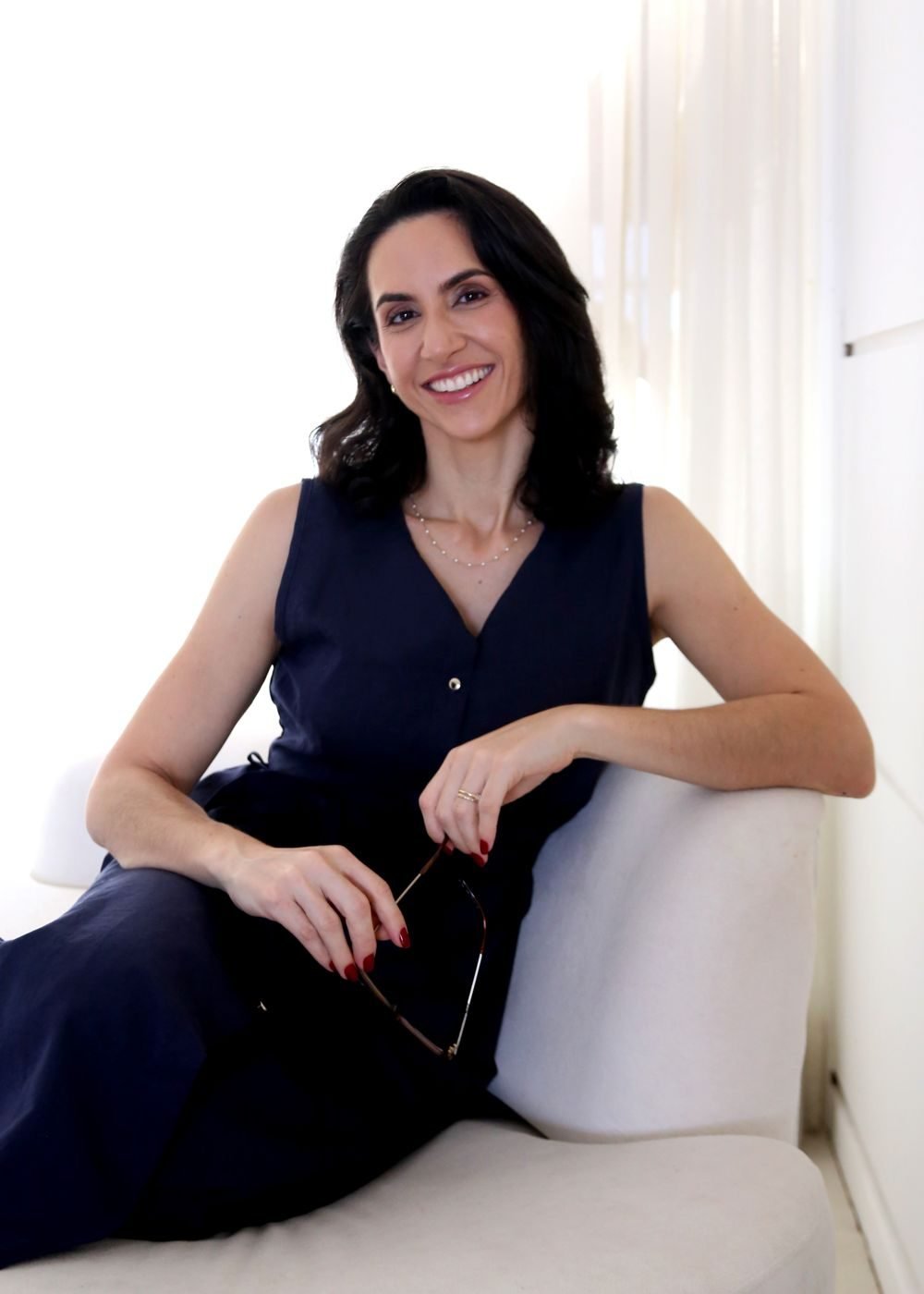 Dra. Svenja Lopez sorrindo, sentada em sofá claro no consultório