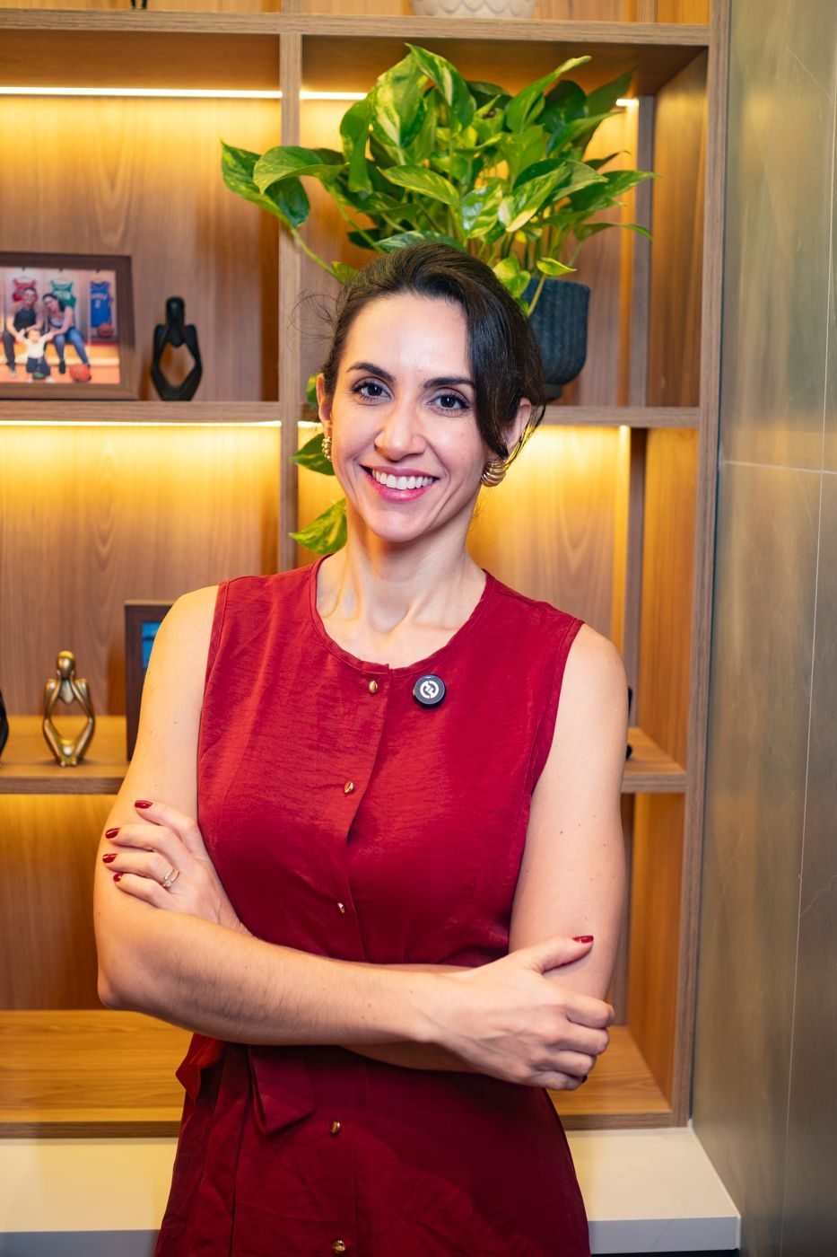 Dra. Svenja Lopez de vestido vermelho, braços cruzados e sorrindo, diante de uma estante iluminada